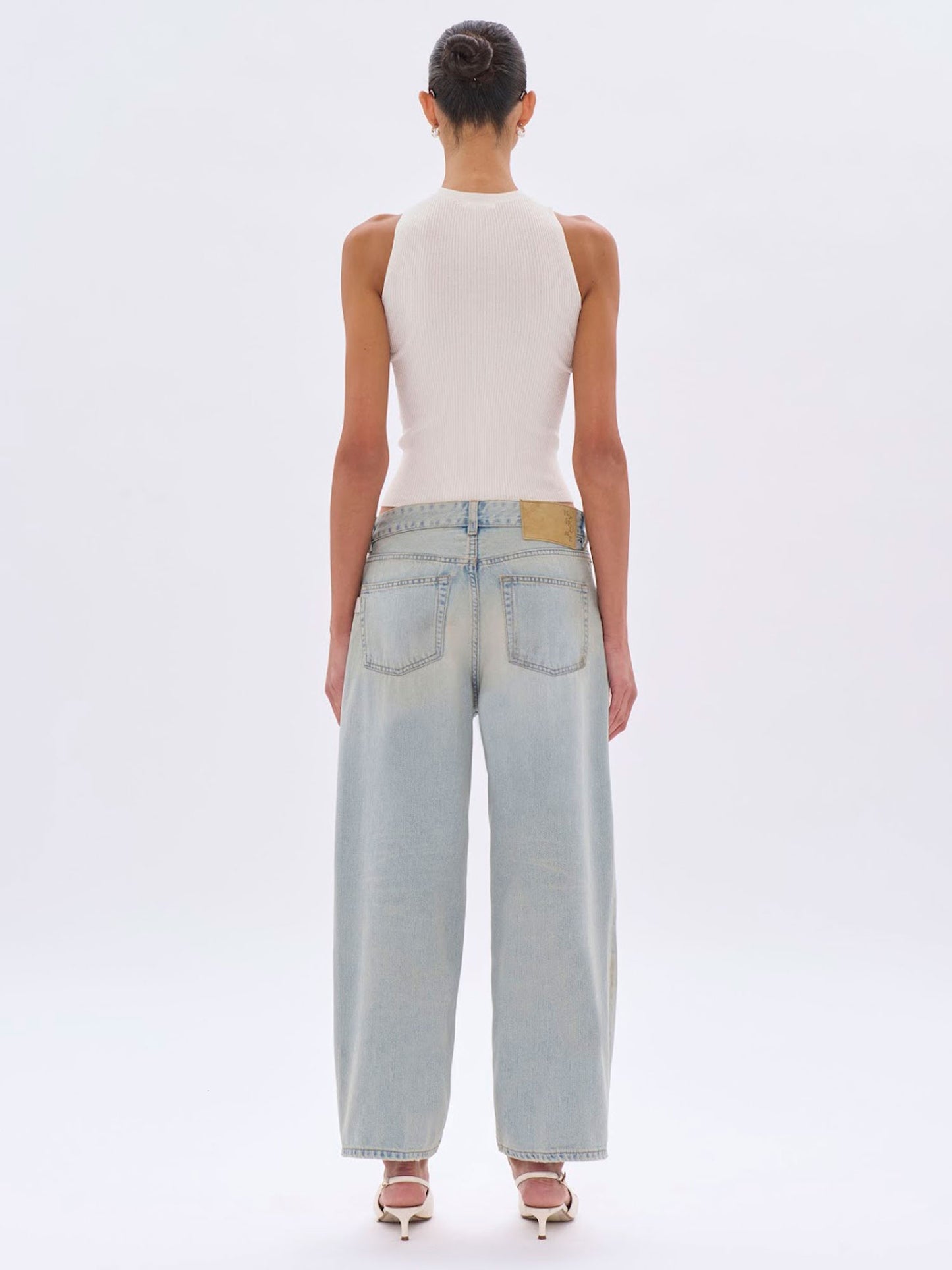 Person wearing light blue jeans and a white sleeveless top on a white background