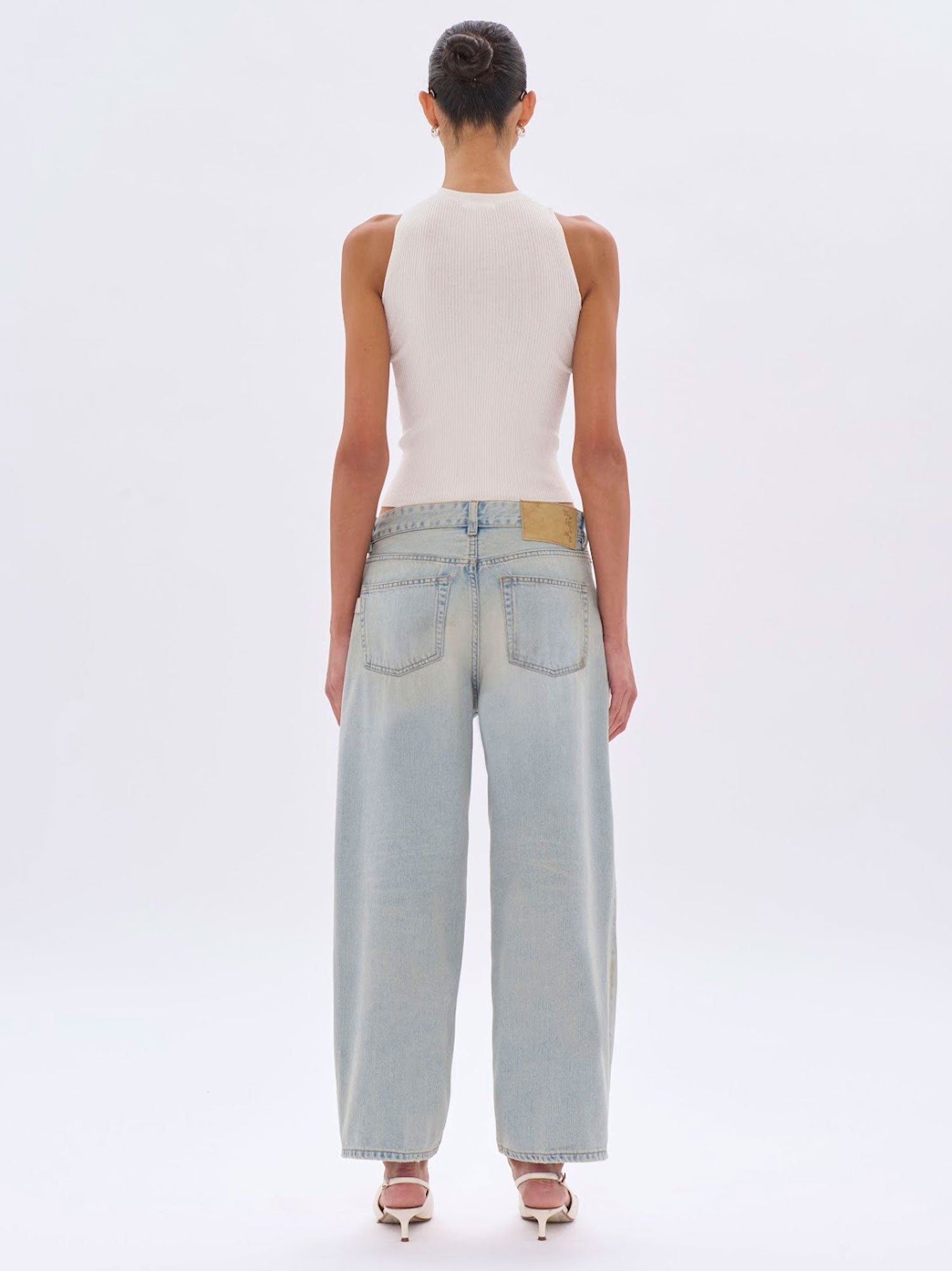 Person wearing light blue jeans and a white sleeveless top on a white background
