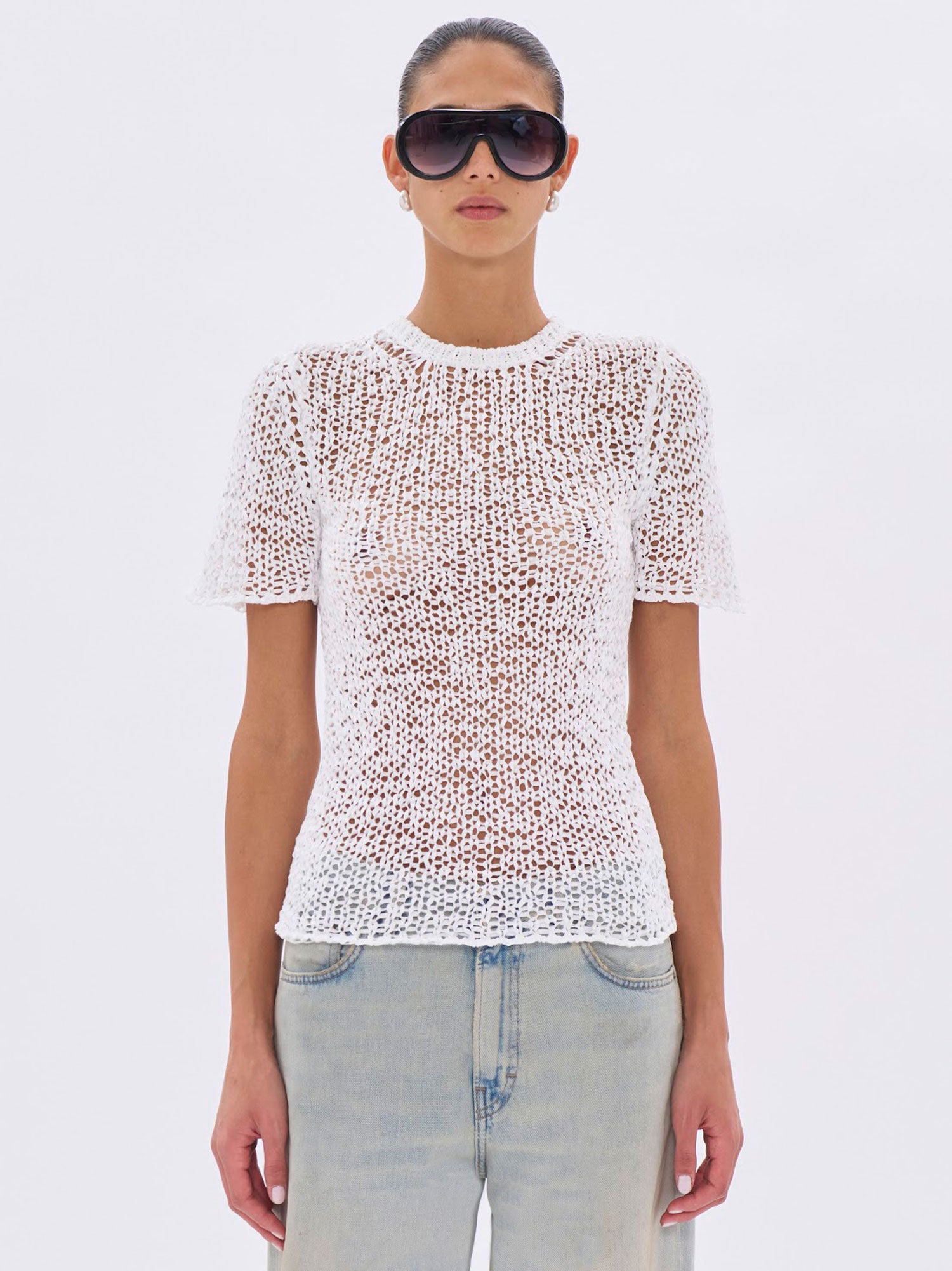 Person wearing a white textured top and sunglasses on a light gray background