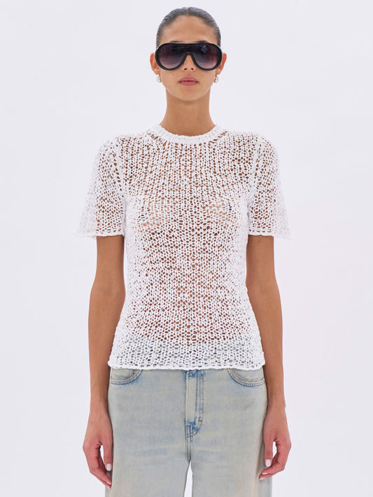 Person wearing a white textured top and sunglasses on a light gray background