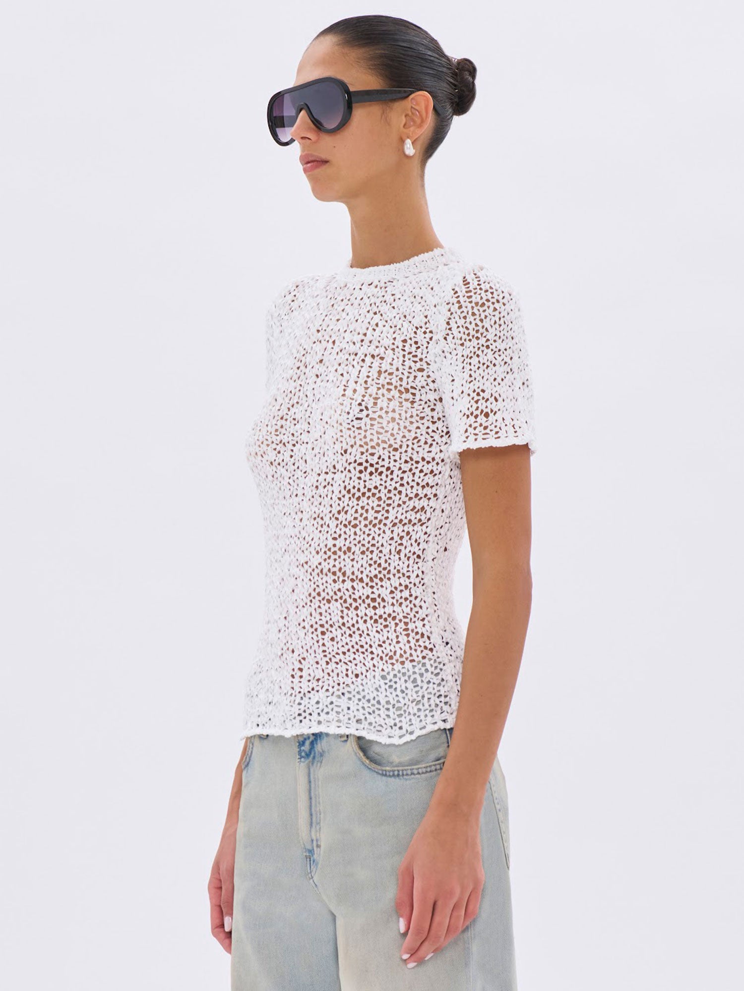 Woman wearing a white textured top and light blue jeans on a white background