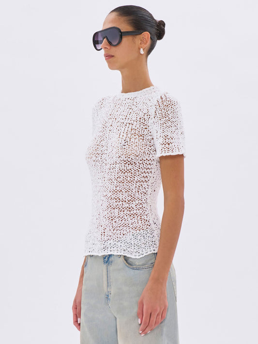 Woman wearing a white textured top and light blue jeans on a white background