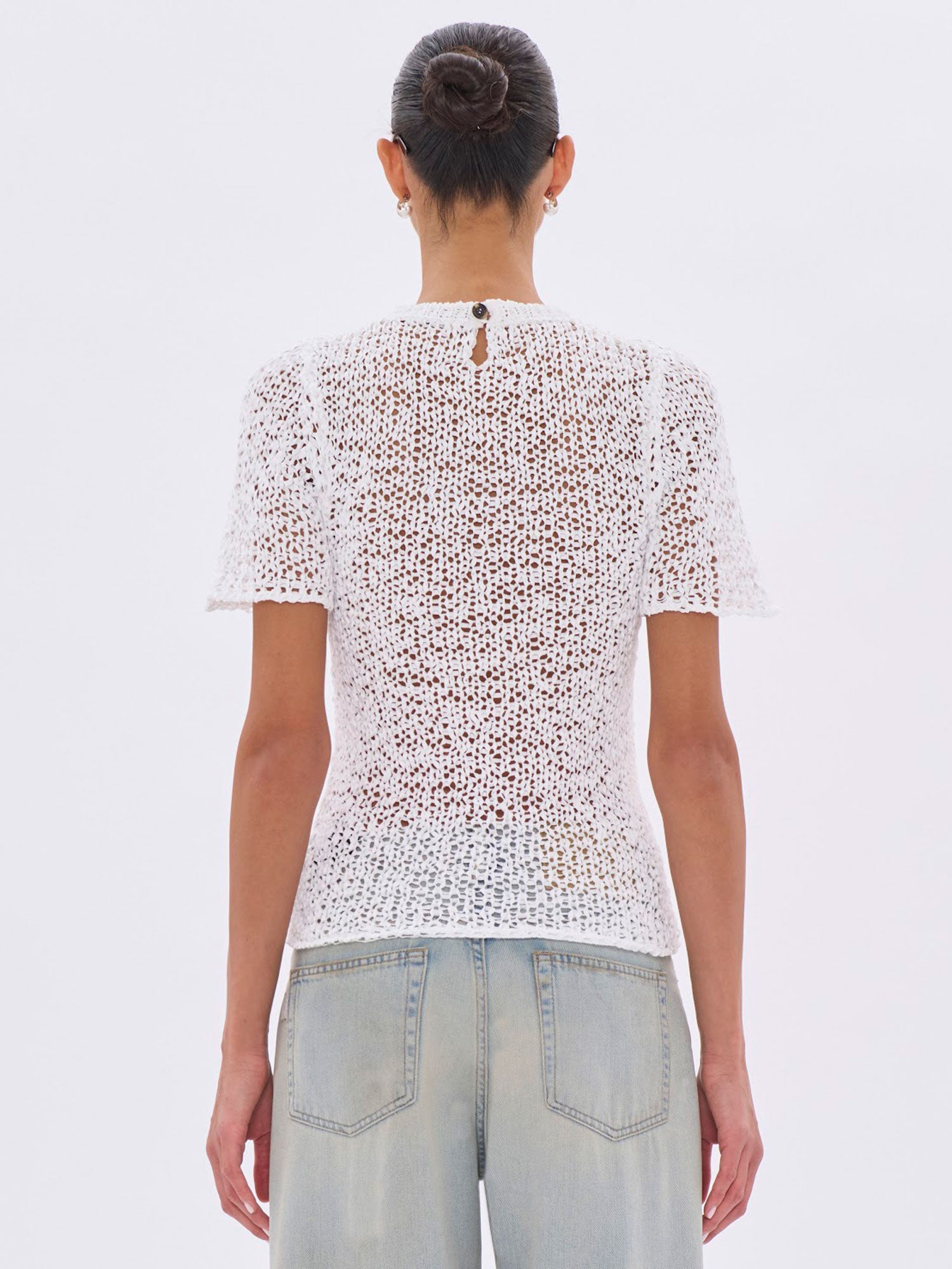 Person wearing a white lace top and light blue jeans on a plain background