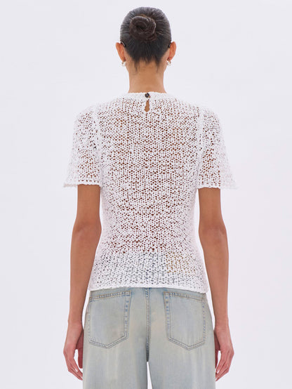 Person wearing a white lace top and light blue jeans on a plain background