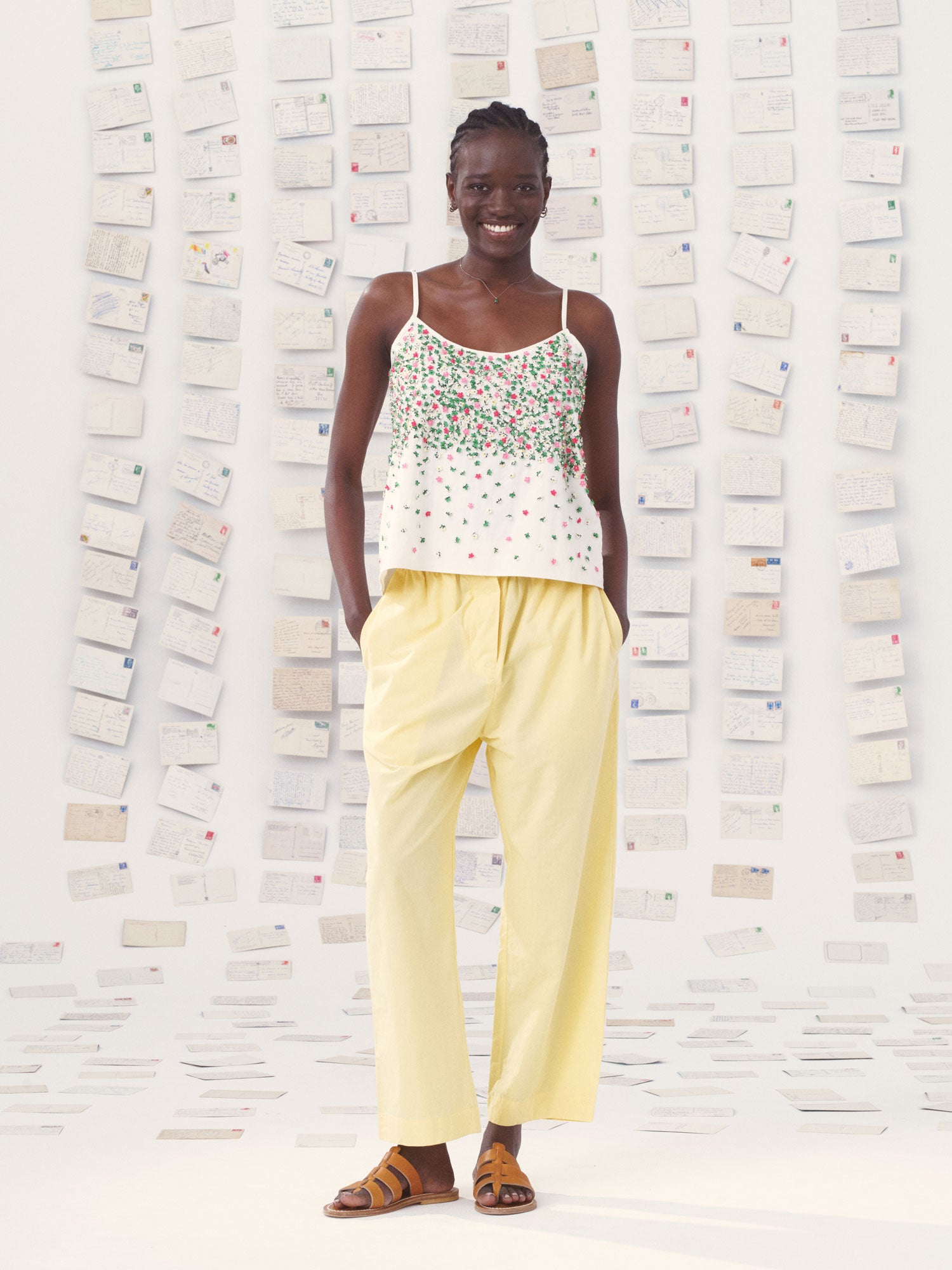 Woman wearing a mii floral top and yellow mii pants standing against a textured white wall.