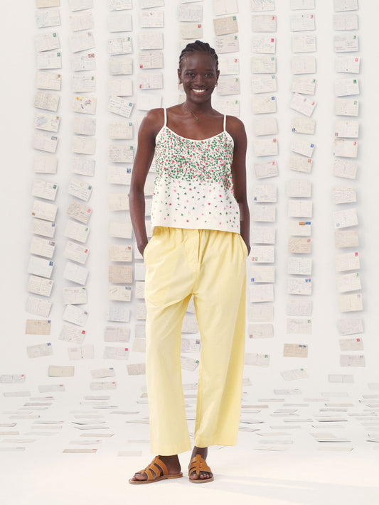Woman wearing a mii floral top and yellow mii pants standing against a textured white wall.