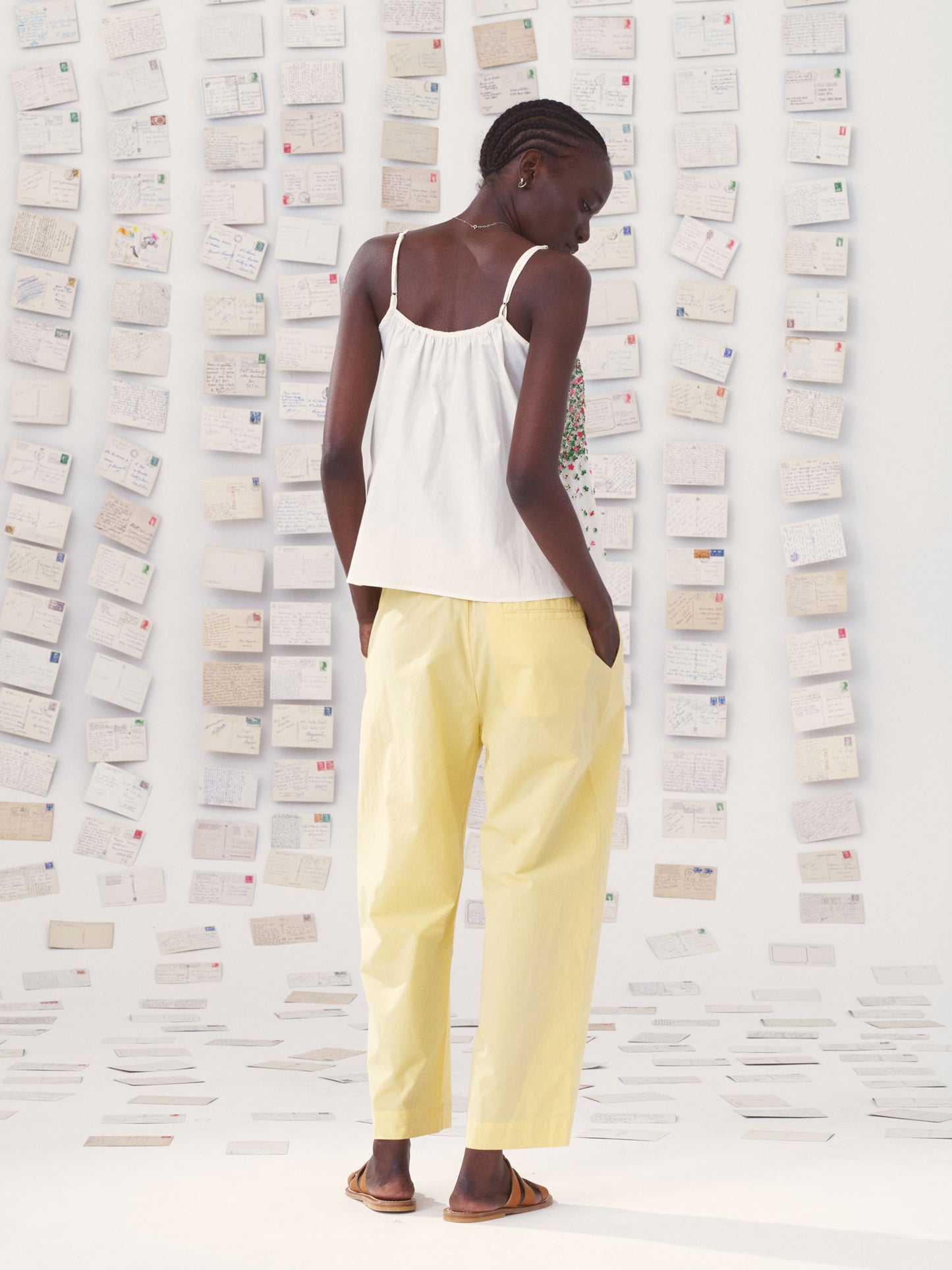 Person wearing a mii white top and yellow mii pants against a textured wall.