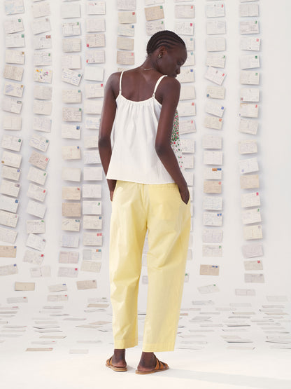 Person wearing a mii white top and yellow mii pants against a textured wall.