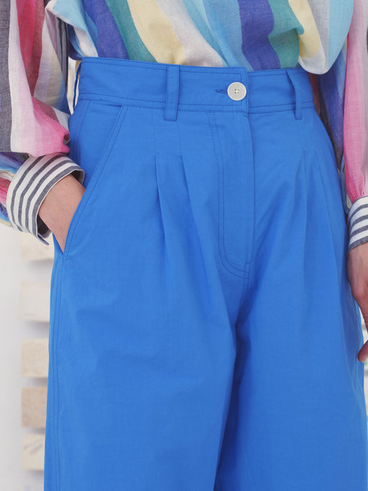 Blue pleated pants worn by a person with a colorful shirt in the background.