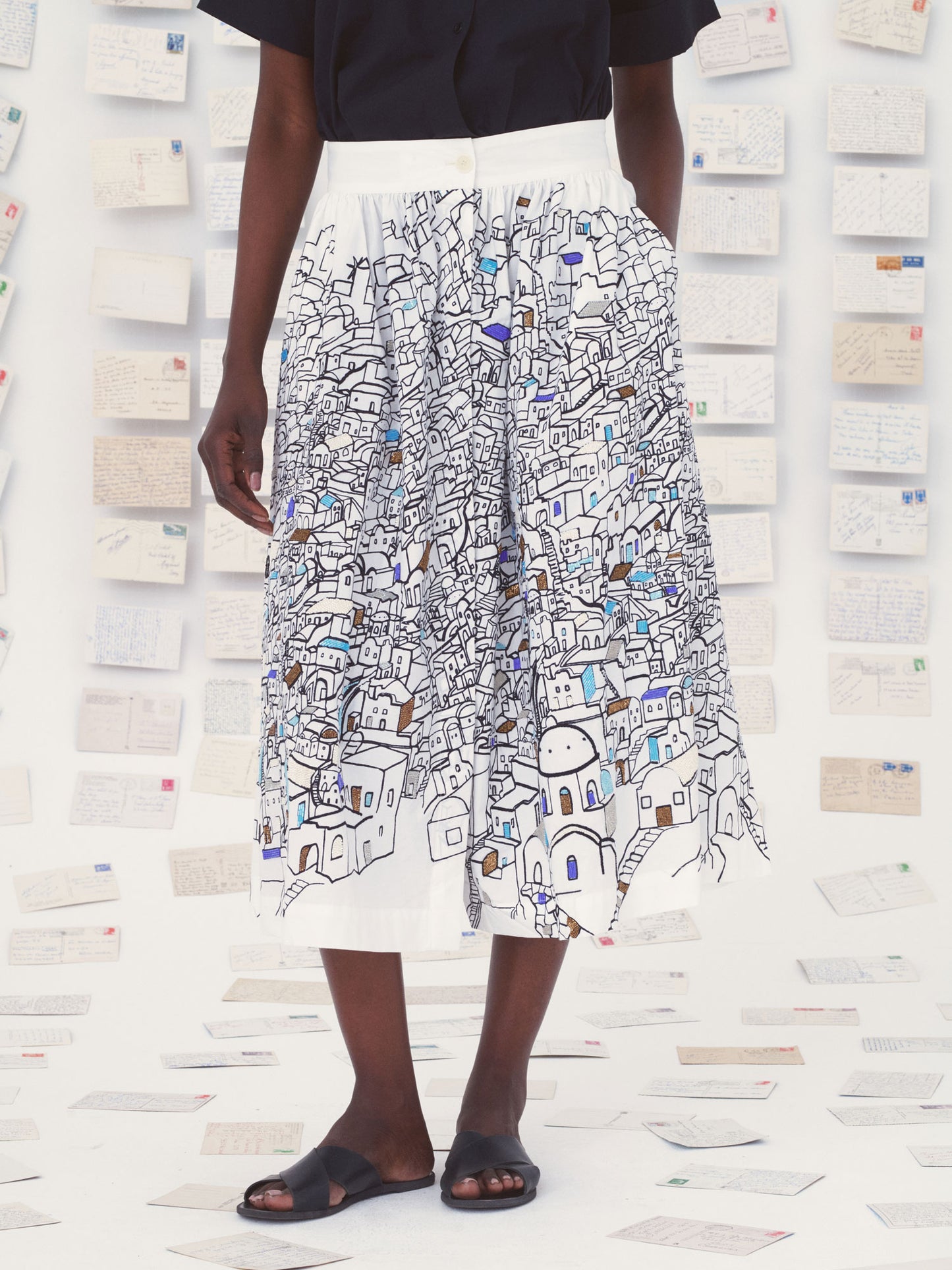 Person wearing a white Mii skirt with colorful patterns against a textured wall.