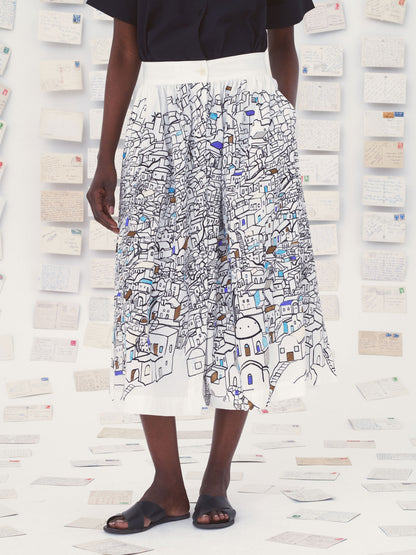 Person wearing a white Mii skirt with colorful patterns against a textured wall.