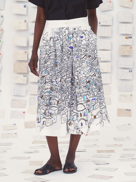 Person wearing a white Mii skirt with colorful patterns against a textured wall.