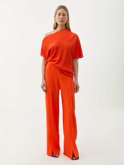 A model wearing a red, asymmetrical, draped top with a loose fit, paired with matching red trousers.