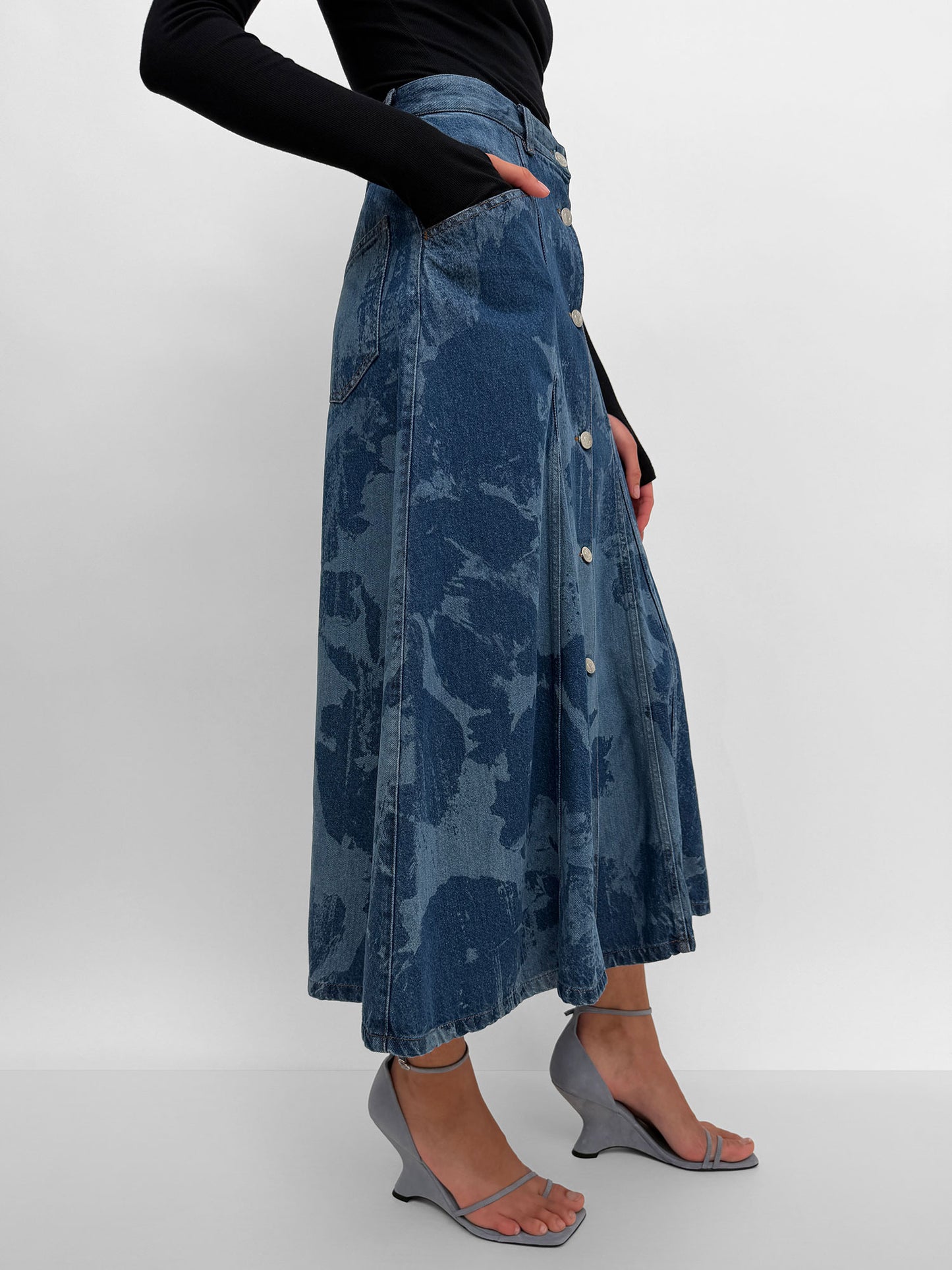 Person wearing a long denim skirt with a plain background