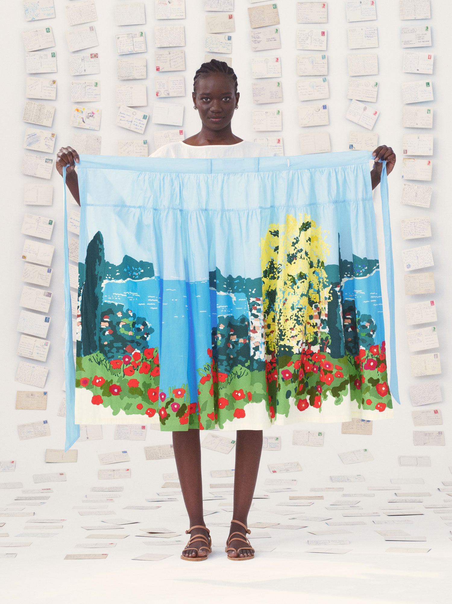 Person holding a colorful Mii skirt with a scenic design against a textured wall.
