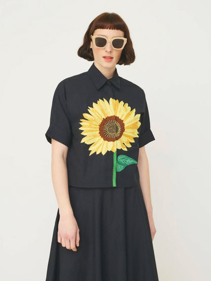 Person wearing a black Mii shirt with a sunflower design on a plain background