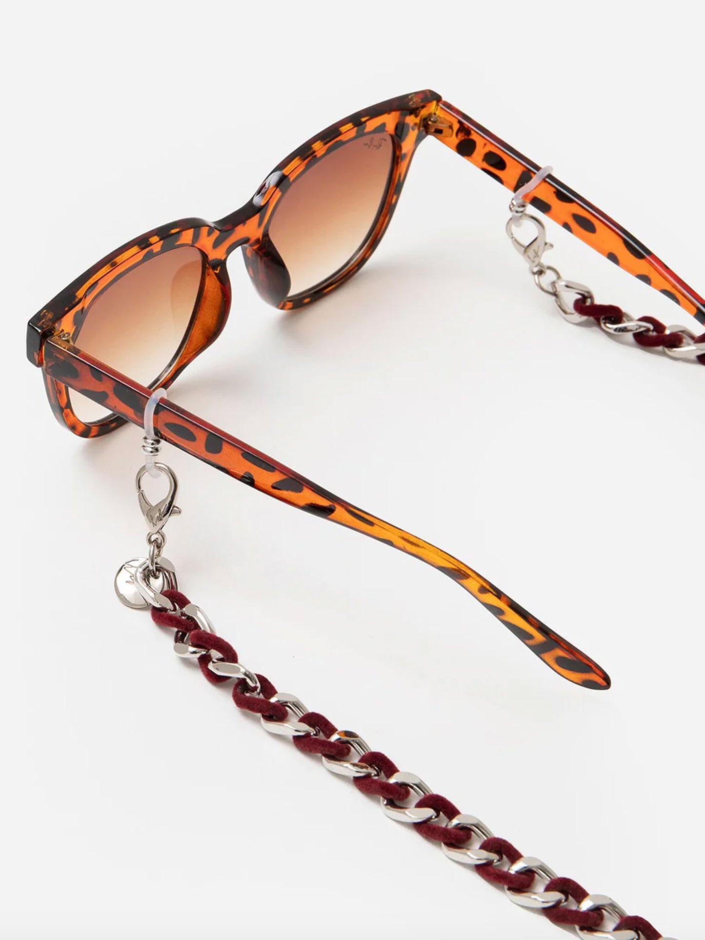 Sunglasses with a leopard print frame and a red and silver chain strap on a white background