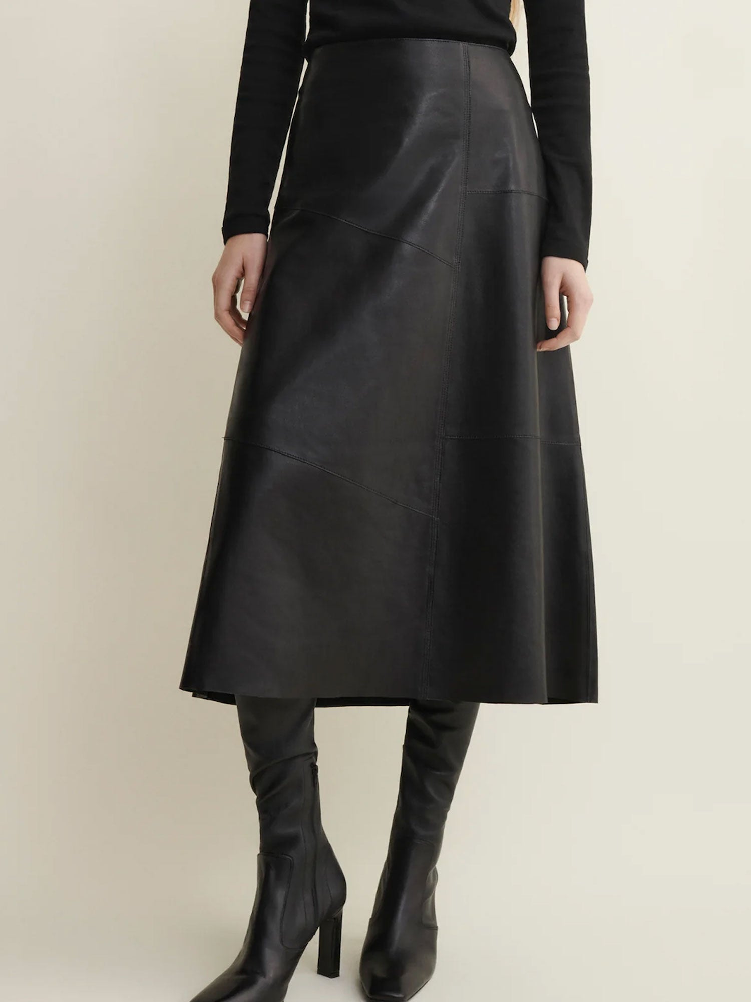 Person wearing a black leather skirt and boots on a beige background