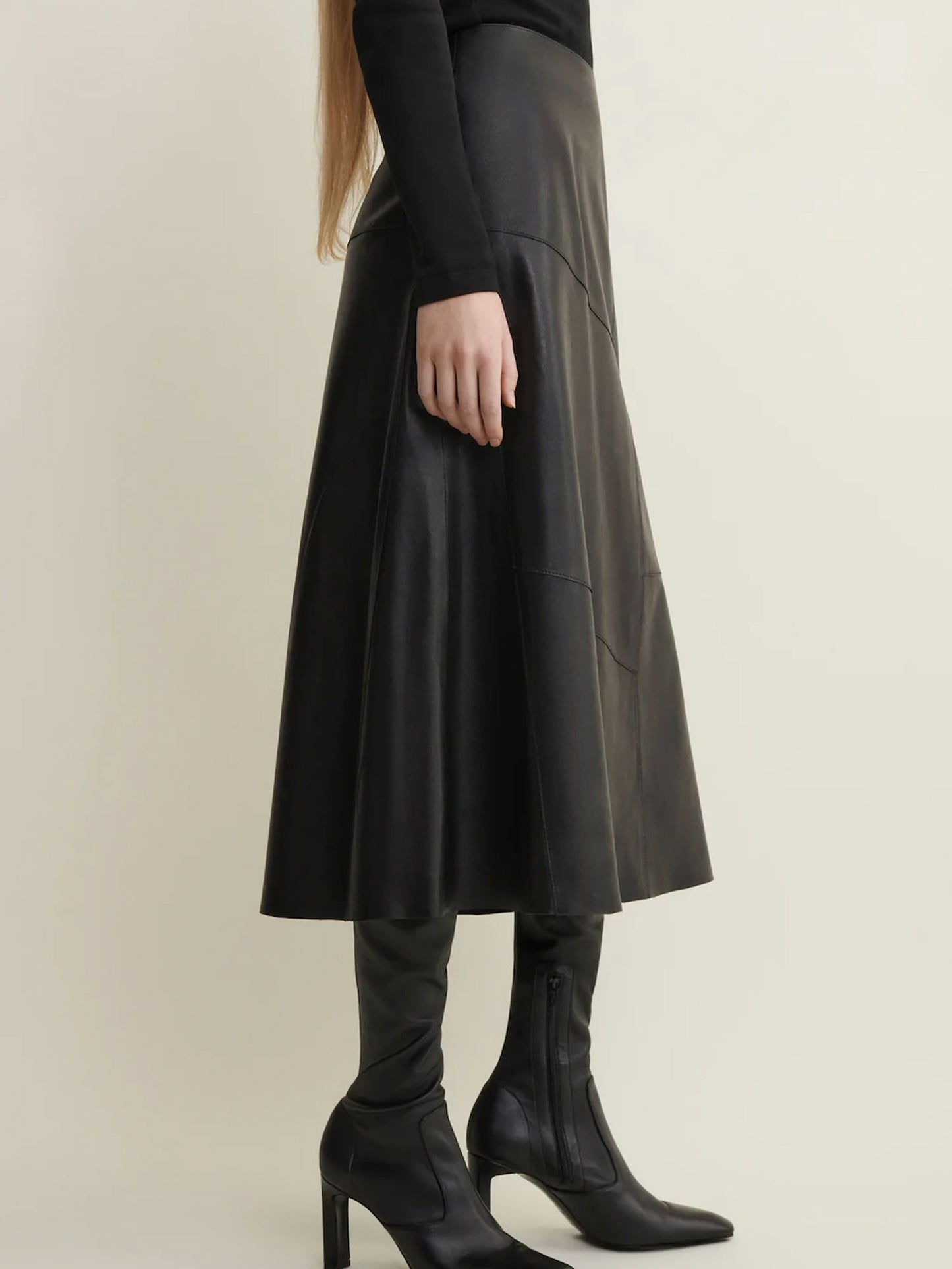 Person wearing a black leather skirt and high-heeled boots on a beige background