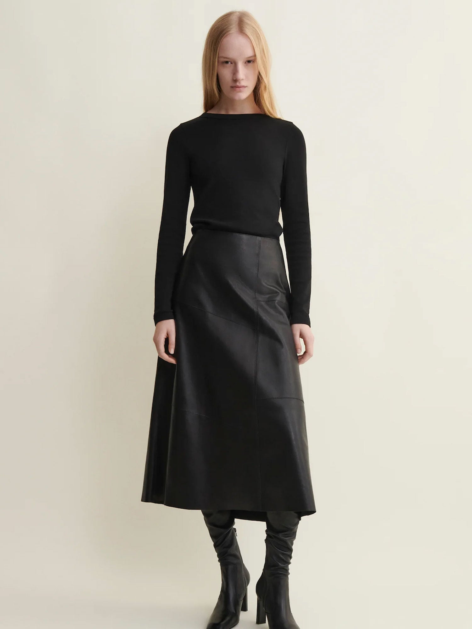 Woman wearing a black long-sleeve top and black leather skirt on a light beige background