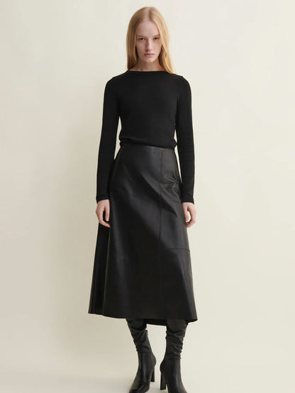 Woman wearing a black long-sleeve top and black leather skirt on a light beige background