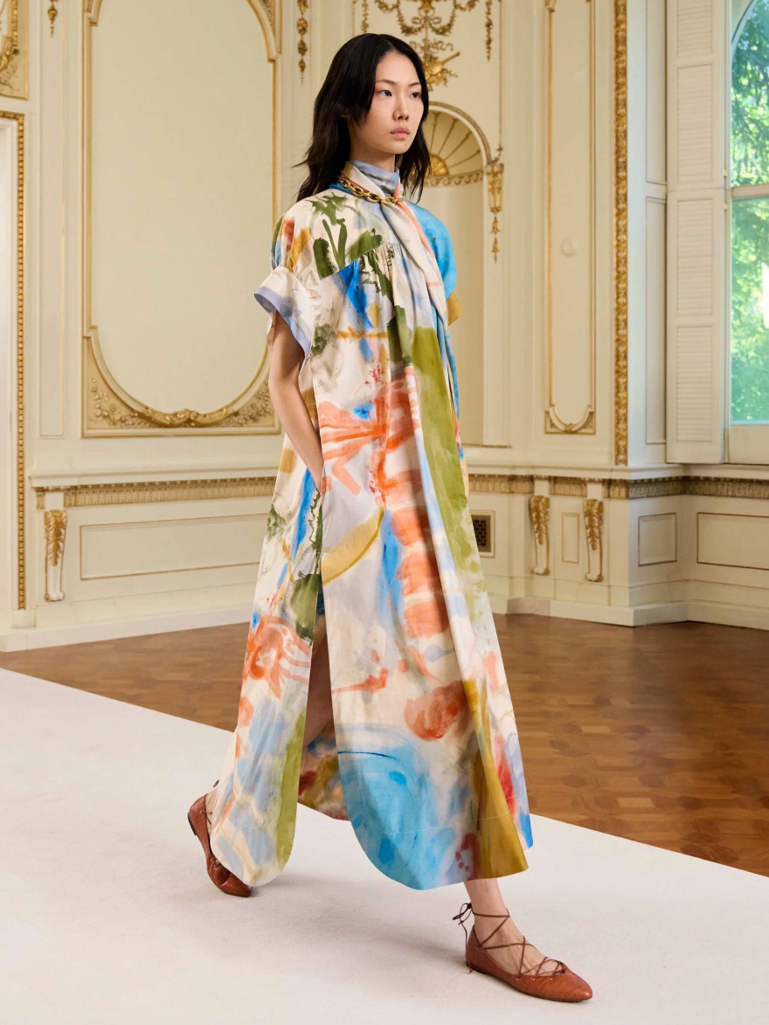 Woman wearing a colorful dress in an elegant room with ornate decor.