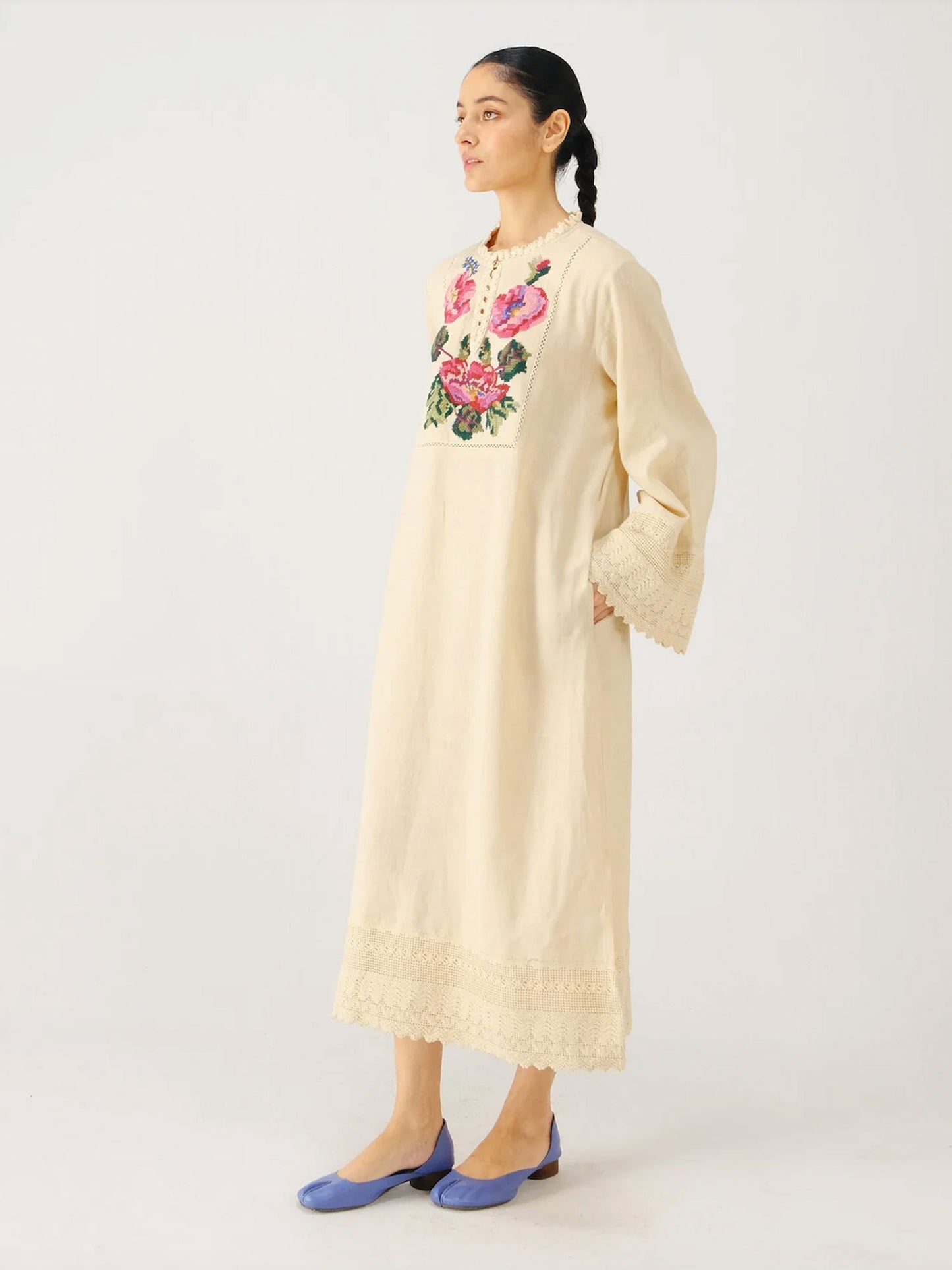 Woman wearing a long beige dress with floral embroidery on a white background
