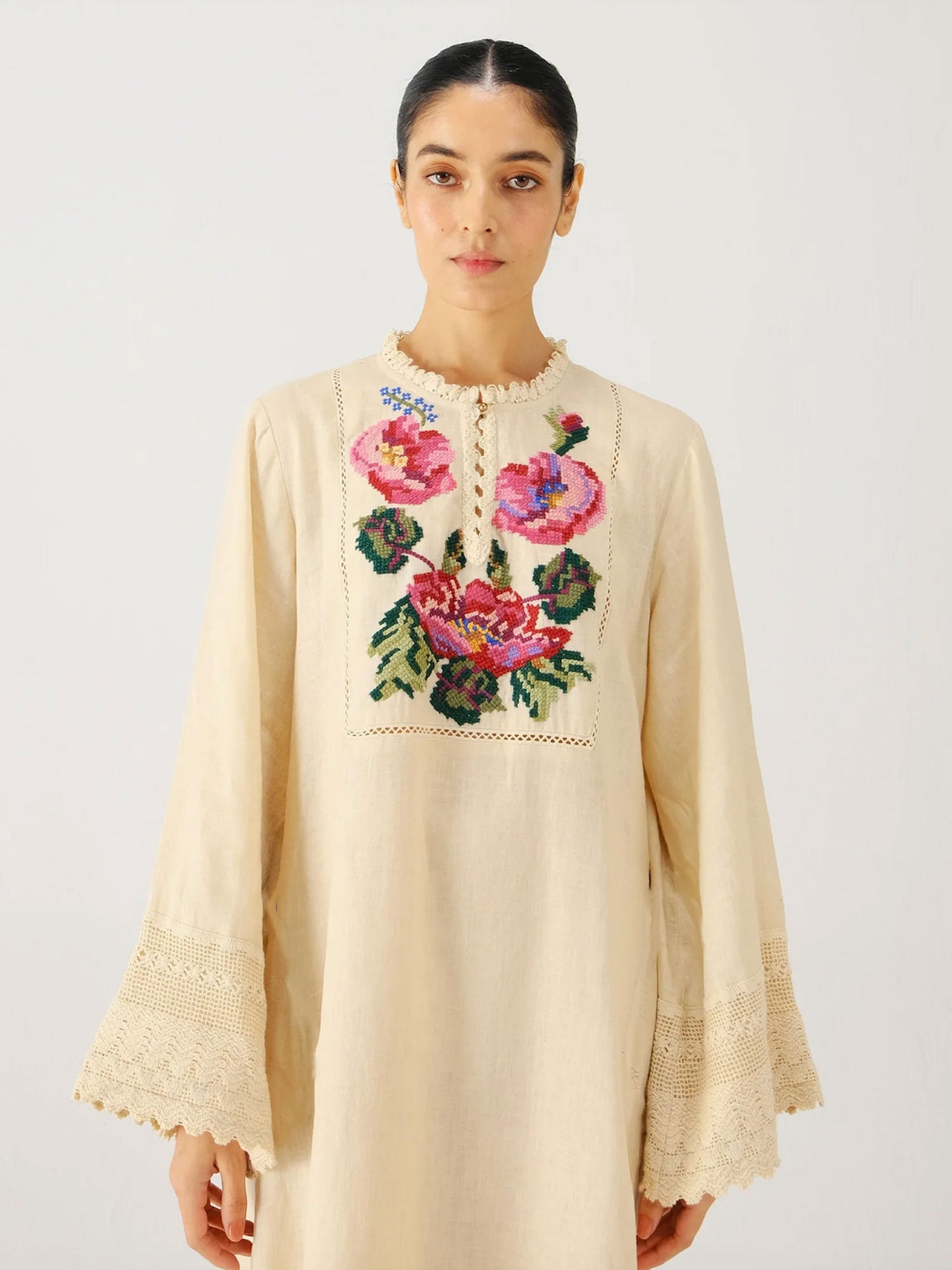 Woman wearing a beige embroidered dress with floral patterns on a white background