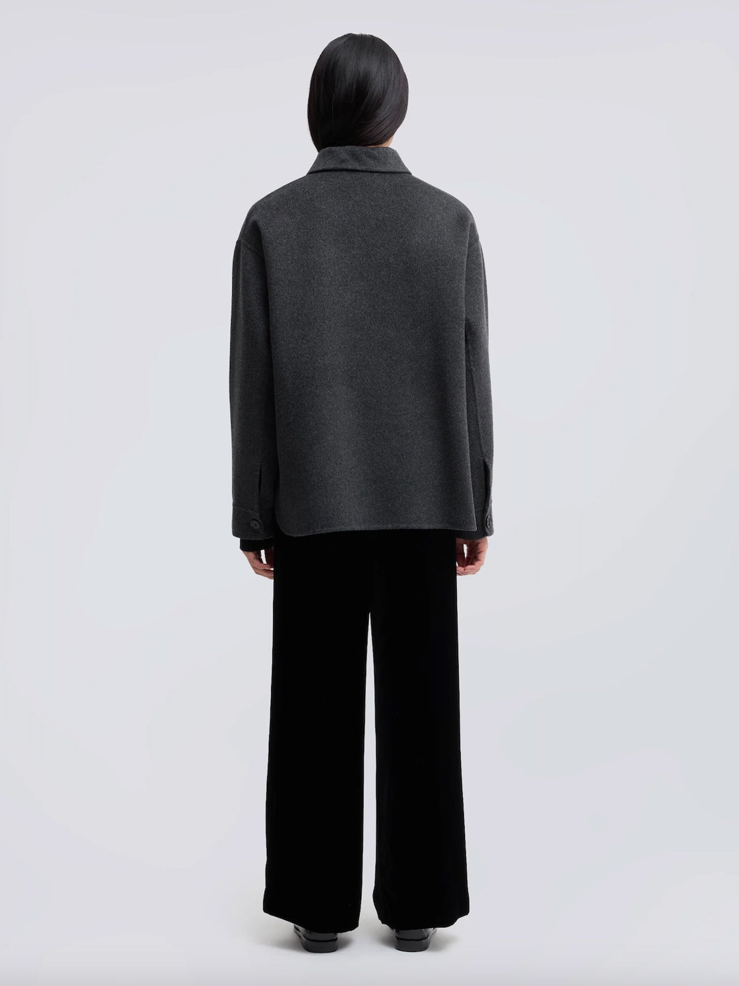 A model shown from the back wearing a dark gray long-sleeve knit top and black wide-leg trousers, photographed against a light gray studio background.