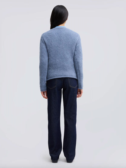 A model viewed from the back wearing a light blue knit sweater and dark blue jeans against a light gray studio background.