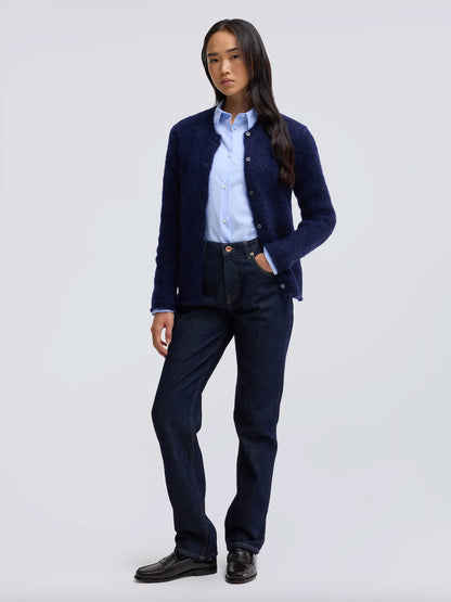 A woman modeling a dark navy blue textured cardigan over a light blue button-down shirt, paired with dark blue jeans and black leather shoes, against a light gray studio background.
