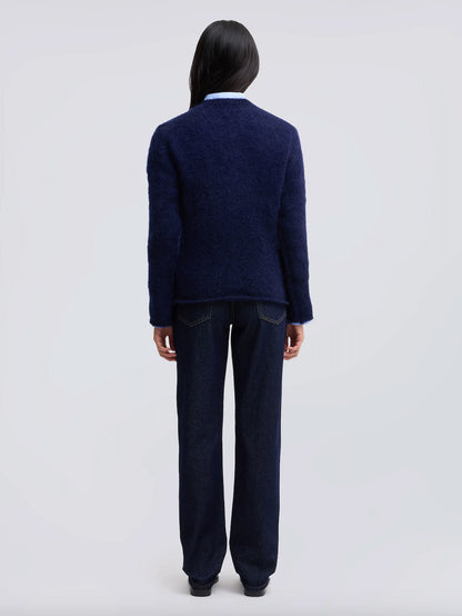 A model viewed from the back wearing a dark navy blue textured knit cardigan over a light blue collared shirt and dark navy wide-leg jeans, set against a plain light gray studio background.