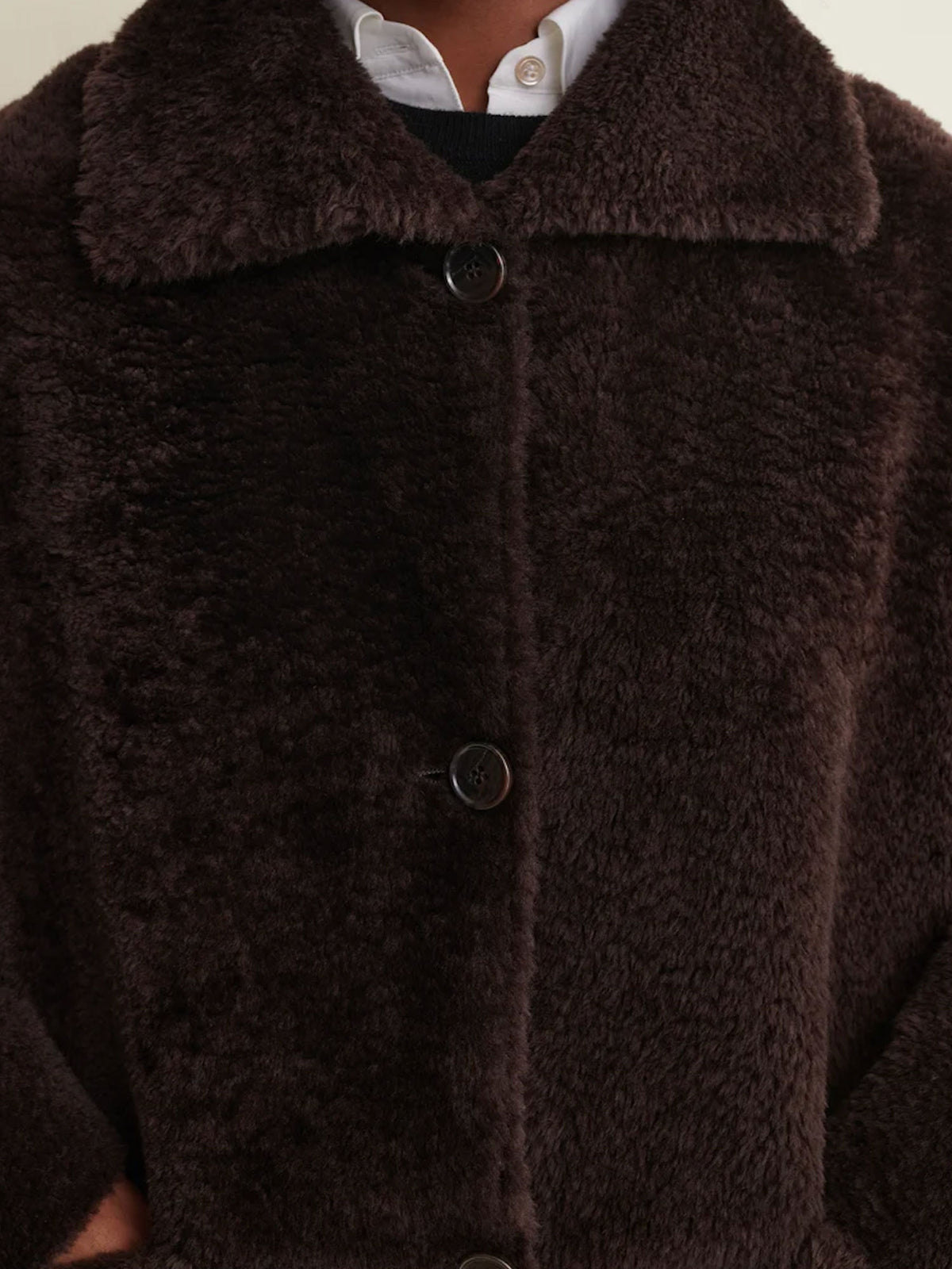 Close-up of a dark brown fuzzy teddy coat with a wide collar and dark buttons, worn over a white collared shirt.