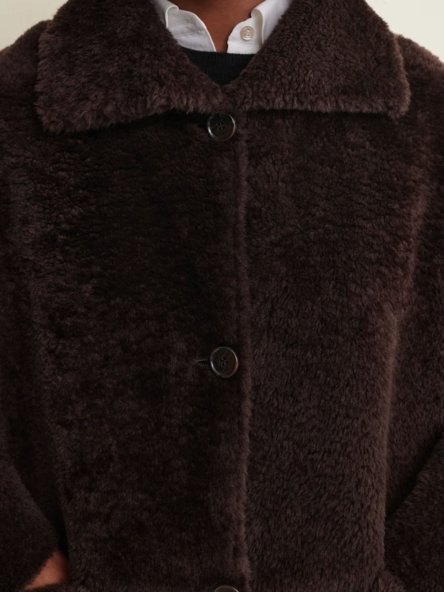 Close-up of a dark brown fuzzy teddy coat with a wide collar and dark buttons, worn over a white collared shirt.