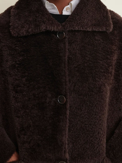 Close-up of a dark brown fuzzy teddy coat with a wide collar and dark buttons, worn over a white collared shirt.
