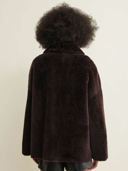 A person shown from the back wearing a dark brown fuzzy teddy-fur style jacket against a plain light beige studio background.