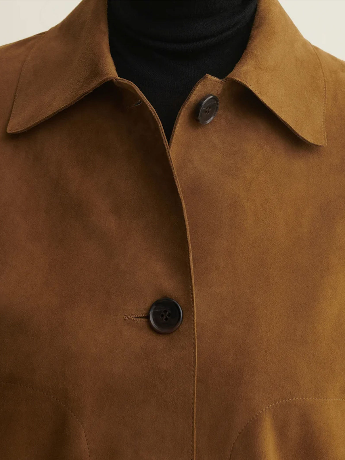 Close-up of a brown suede or nubuck jacket with a collar and dark buttons, worn over a black turtleneck.