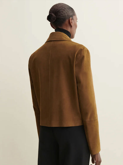 A model shown from the back wearing a cropped, long-sleeve camel brown suede jacket over a black turtleneck and black trousers, set against a plain off-white studio background.