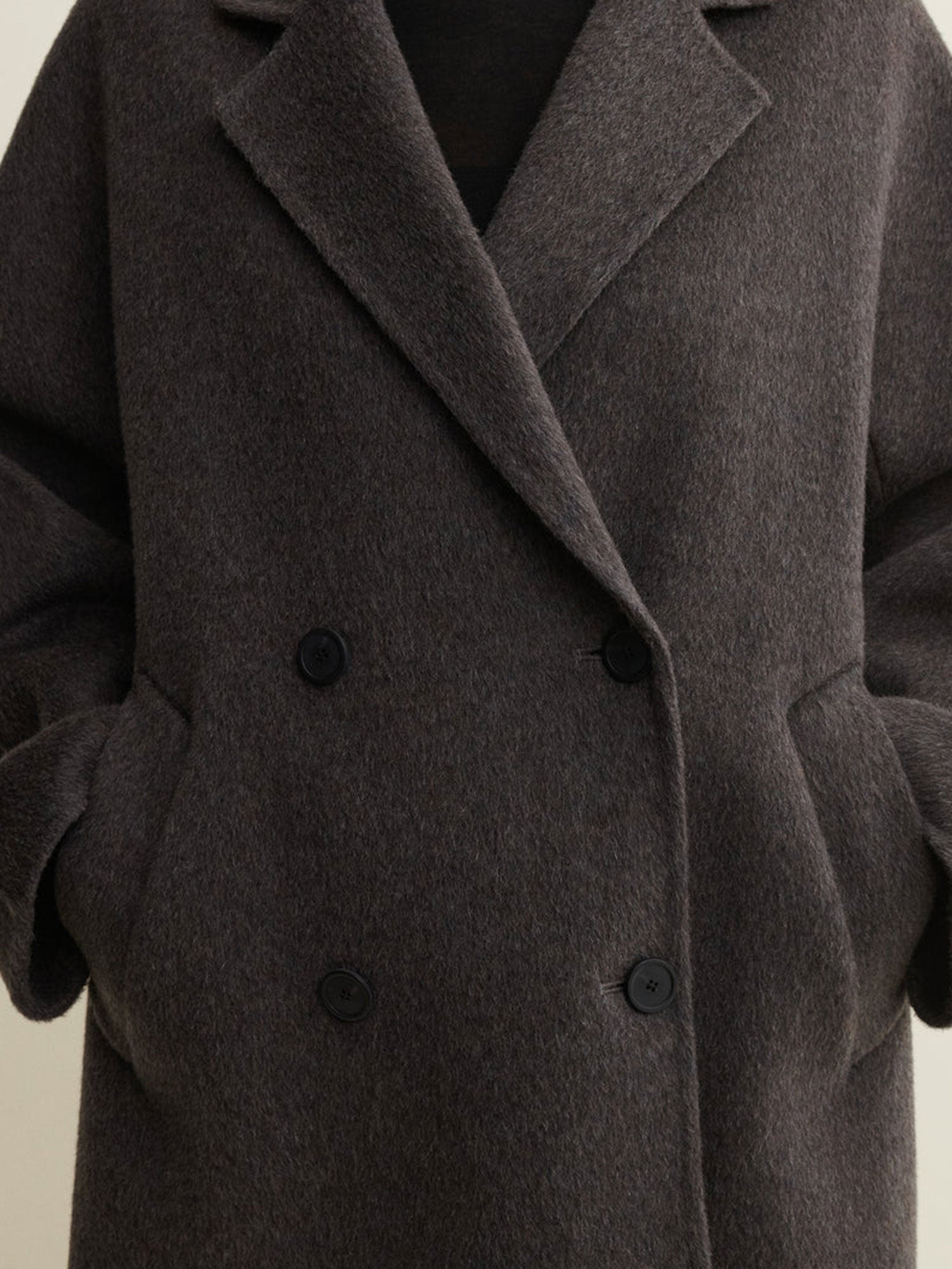 A close-up of a dark brown double-breasted wool coat with a soft, textured finish and black buttons.