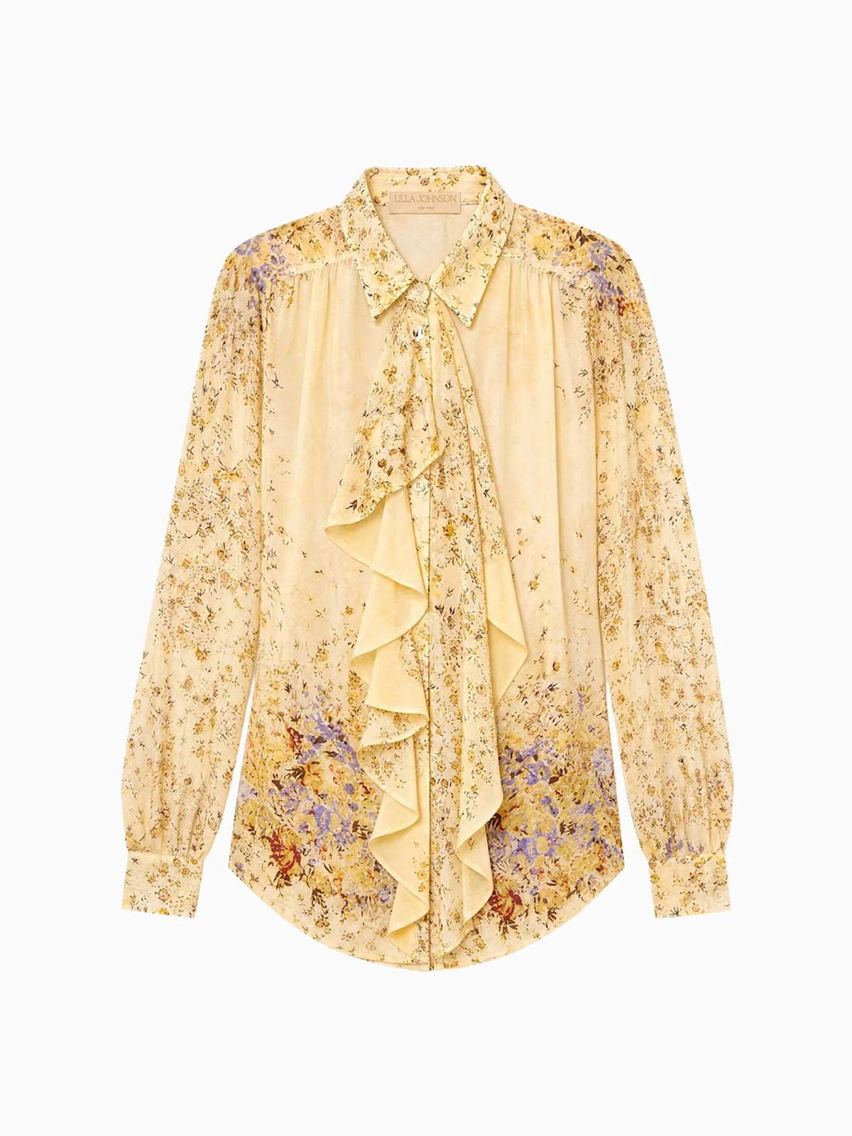 A long-sleeve blouse in pale yellow silk with a dense floral print in gold, brown, and purple, featuring a ruffled tie-neck detail and a curved hem.