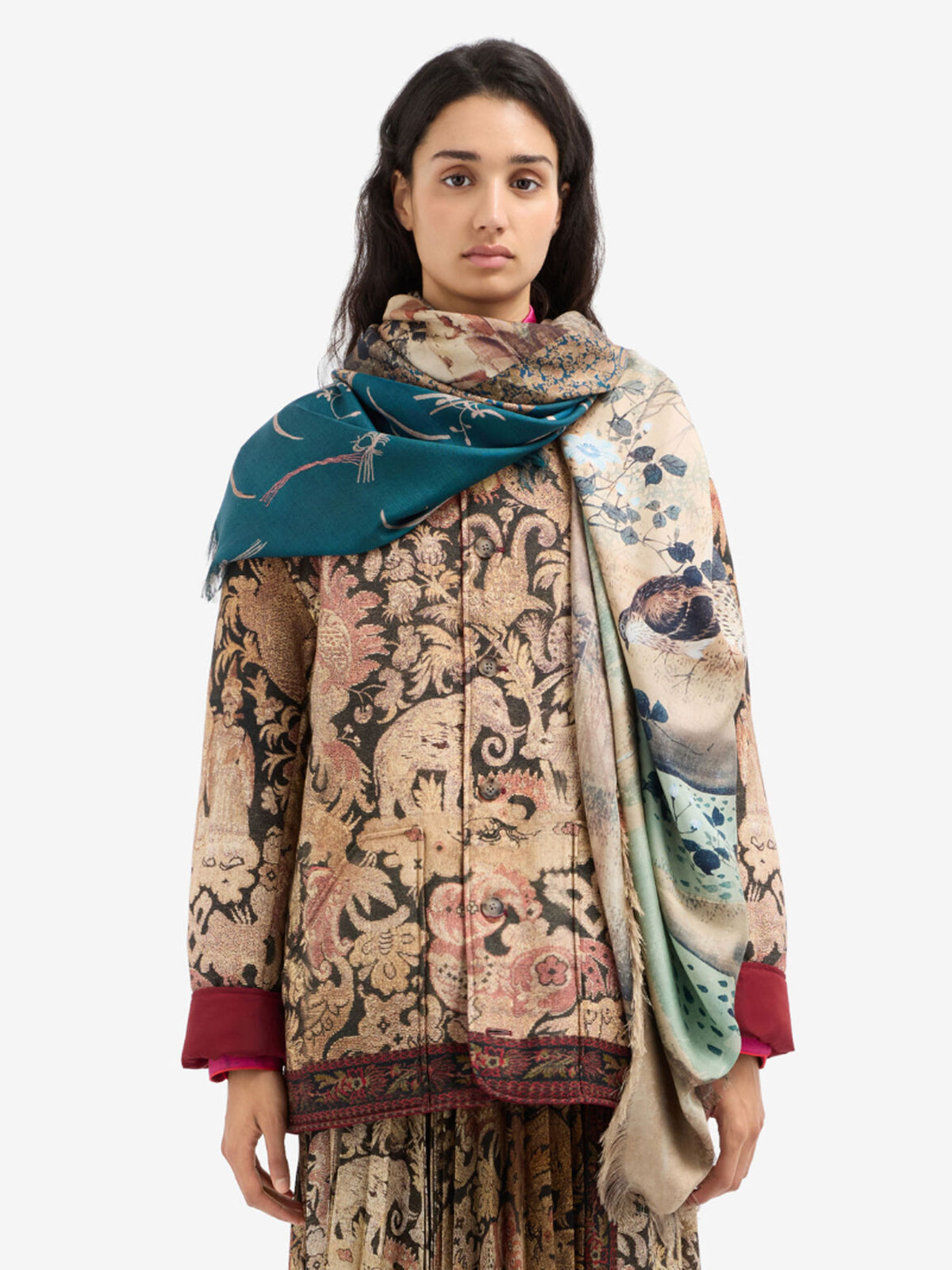 A woman modeling a beige and brown ornate floral print shawl draped over her shoulders, paired with a teal scarf and a matching patterned jacket with burgundy cuffs.