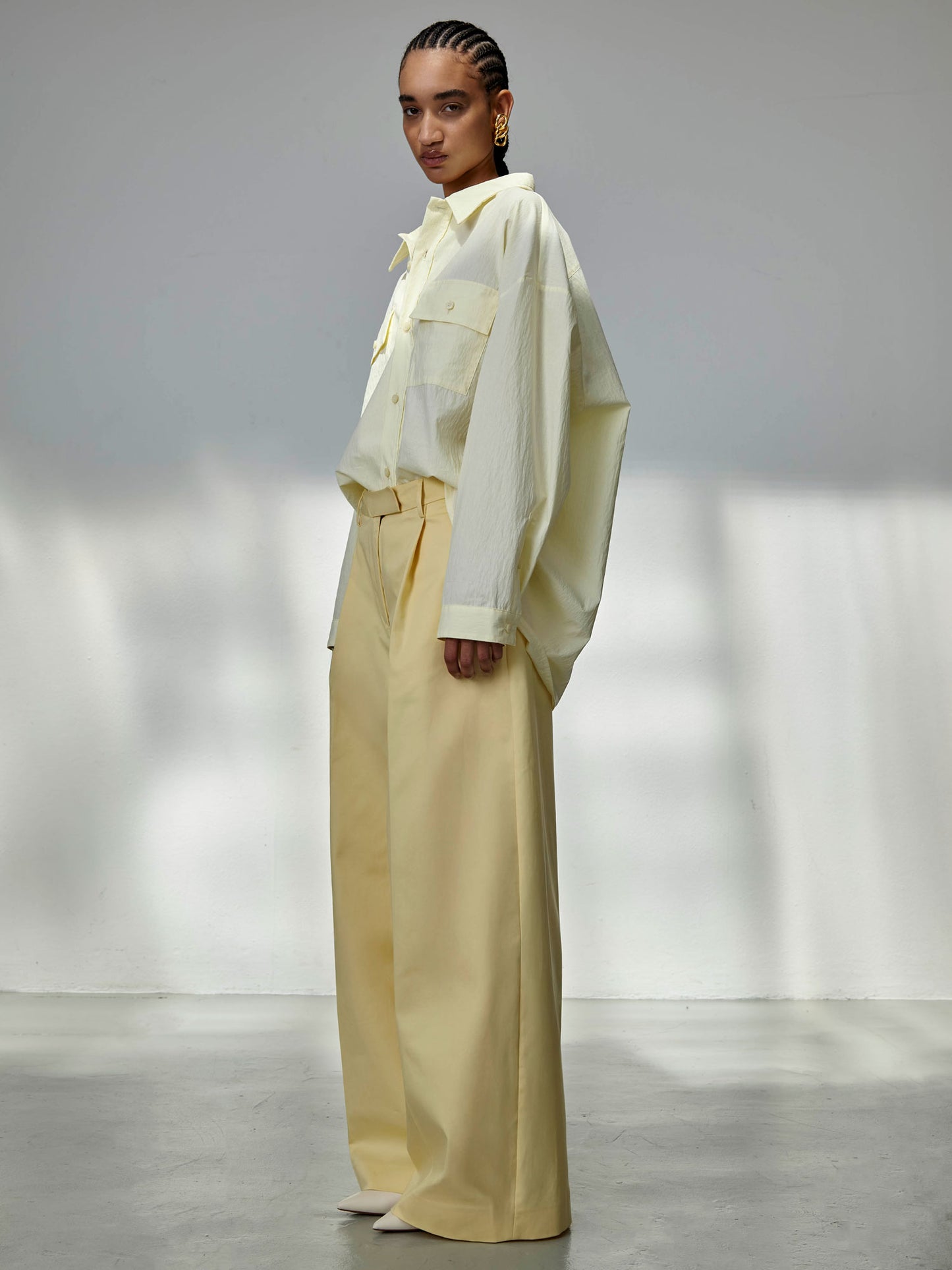 Person wearing a light-colored outfit with a white shirt and beige pants in a minimalistic setting.