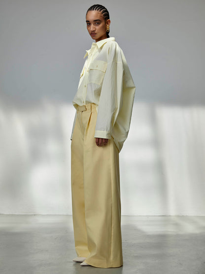 Person wearing a light-colored outfit with a white shirt and beige pants in a minimalistic setting.