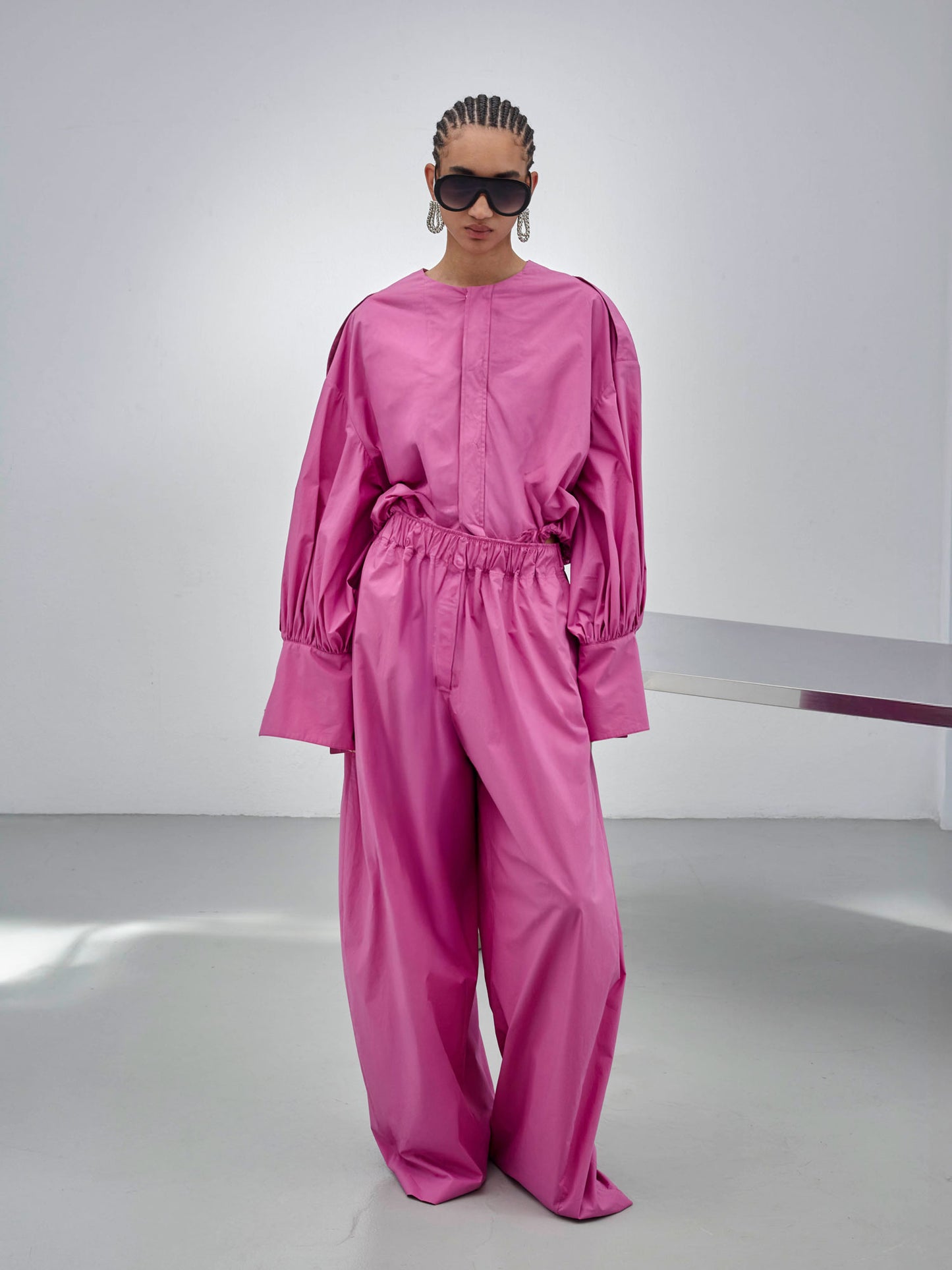 Person wearing a pink outfit with sunglasses in a minimalistic setting