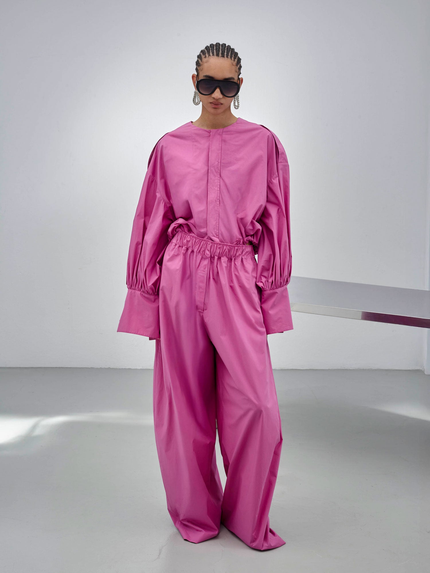 Person wearing a pink outfit with sunglasses in a minimalistic setting