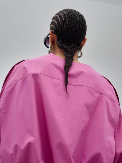 Person wearing a bright pink jacket with braided hair, standing against a plain background