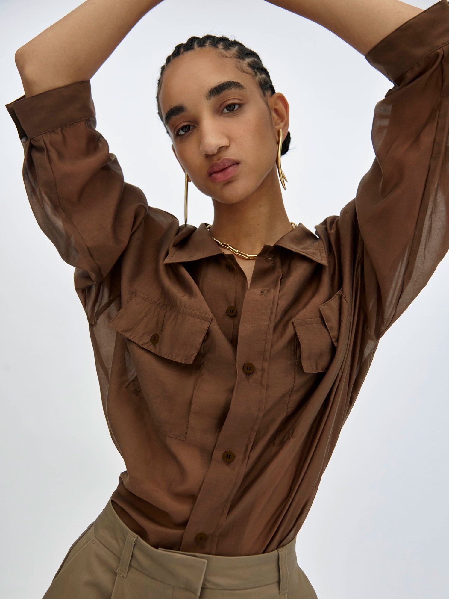 Woman wearing a brown shirt with rolled-up sleeves against a white background