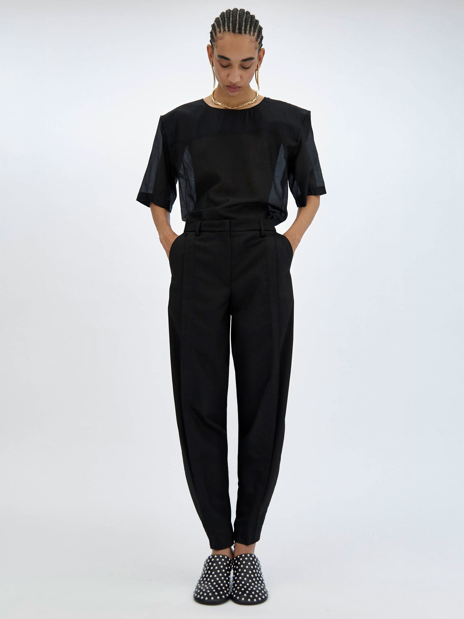 Person wearing a black outfit with high-waisted pants and studded shoes on a white background