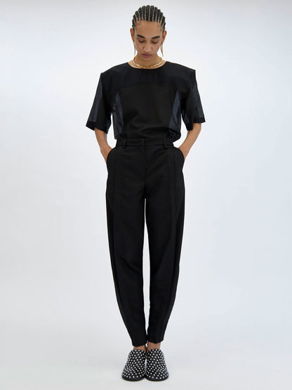 Person wearing a black outfit with high-waisted pants and studded shoes on a white background