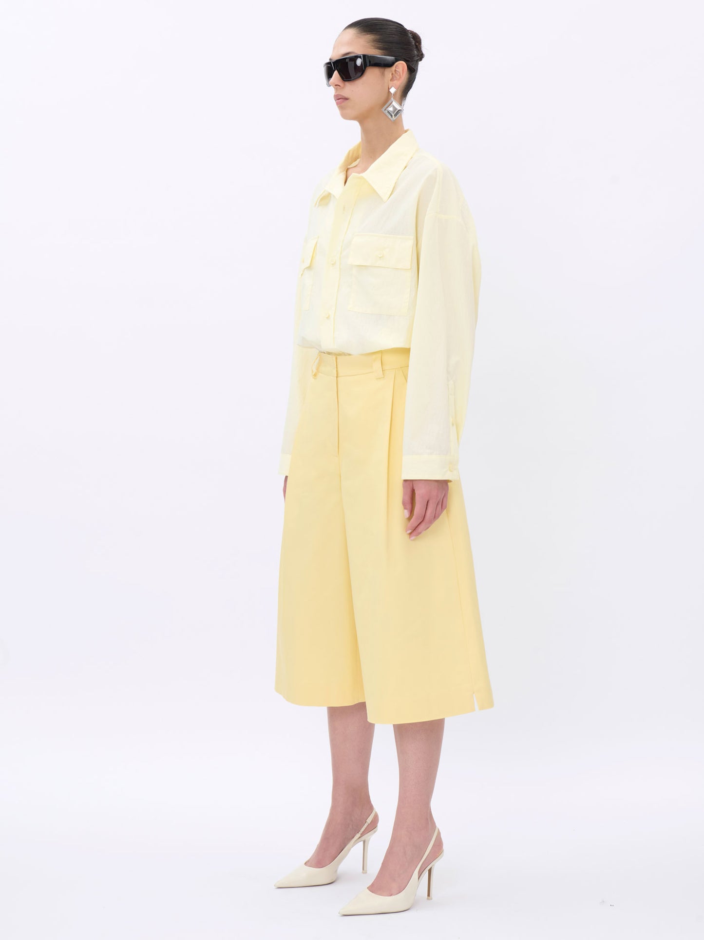Person wearing a light yellow outfit with a shirt, short, and heels on a white background